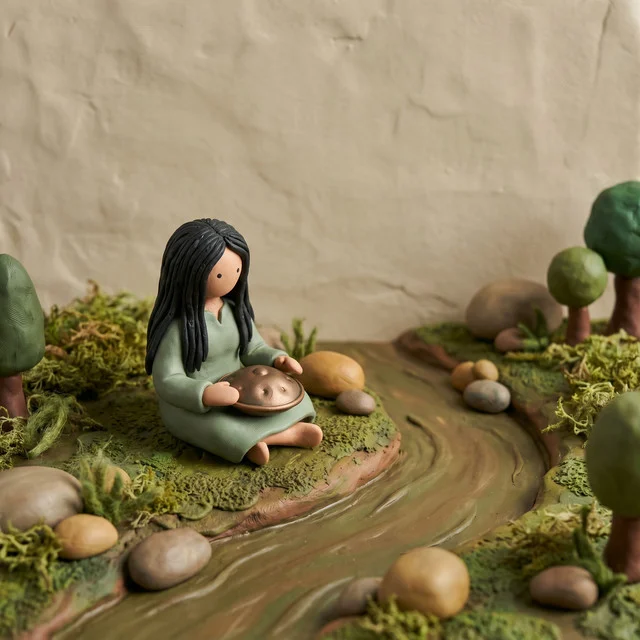 The Slow River cover: the clay figure on a mossy bank beside a river.